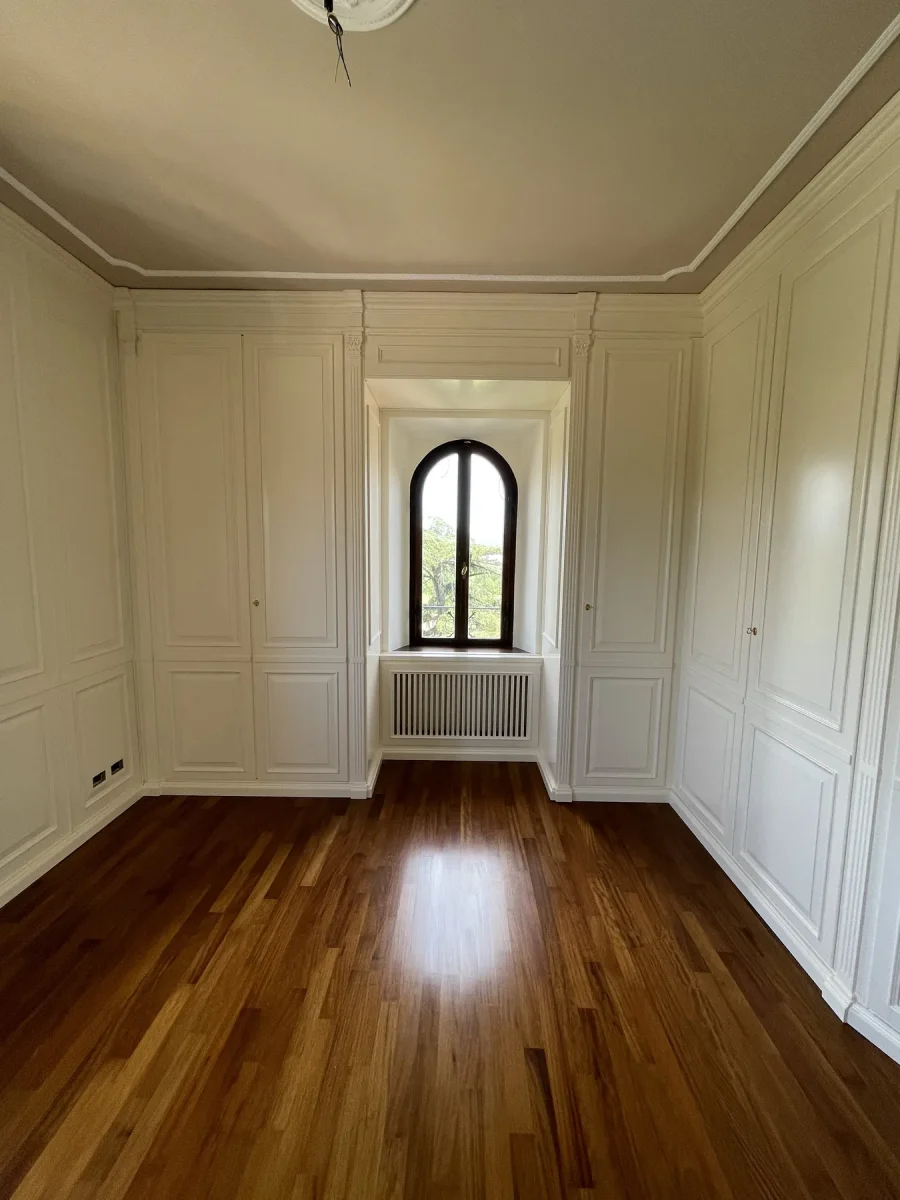 Parete rivestita in doghe di noce accanto alla finestra ad arco e alla boiserie bianca