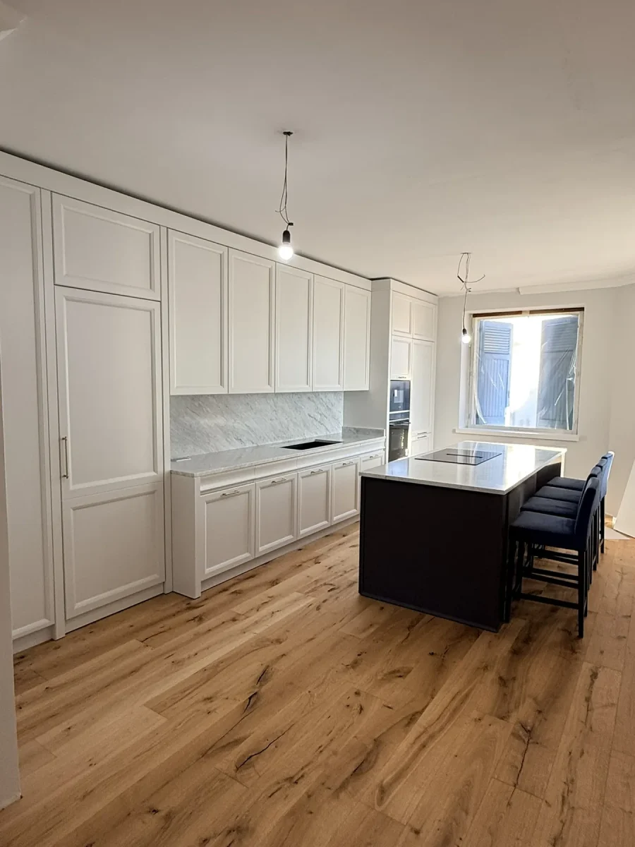 Parete a boiserie laccata avorio fino a soffitto, con pavimento in rovere spazzolato e isola scura