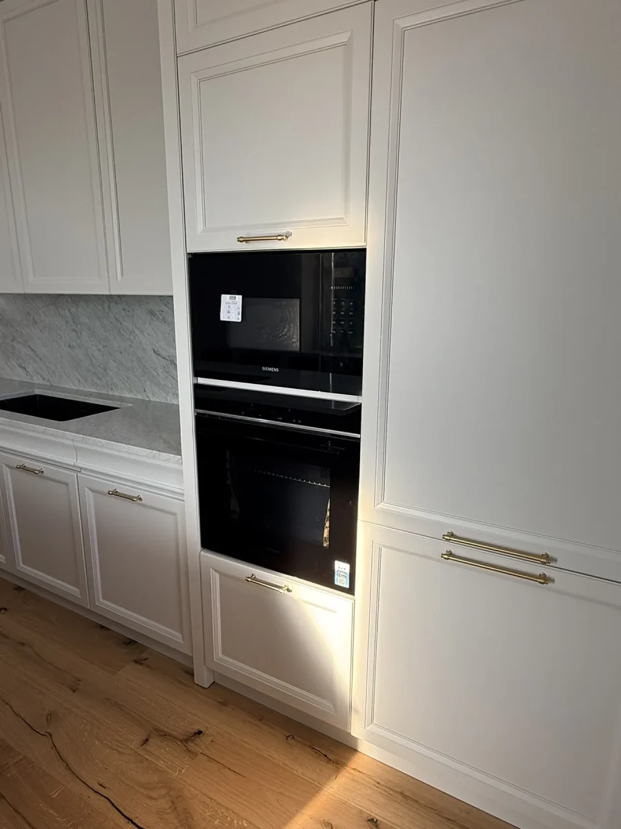 Colonna attrezzata con forno e microonde neri incassati nella boiserie laccata avorio, maniglie in ottone