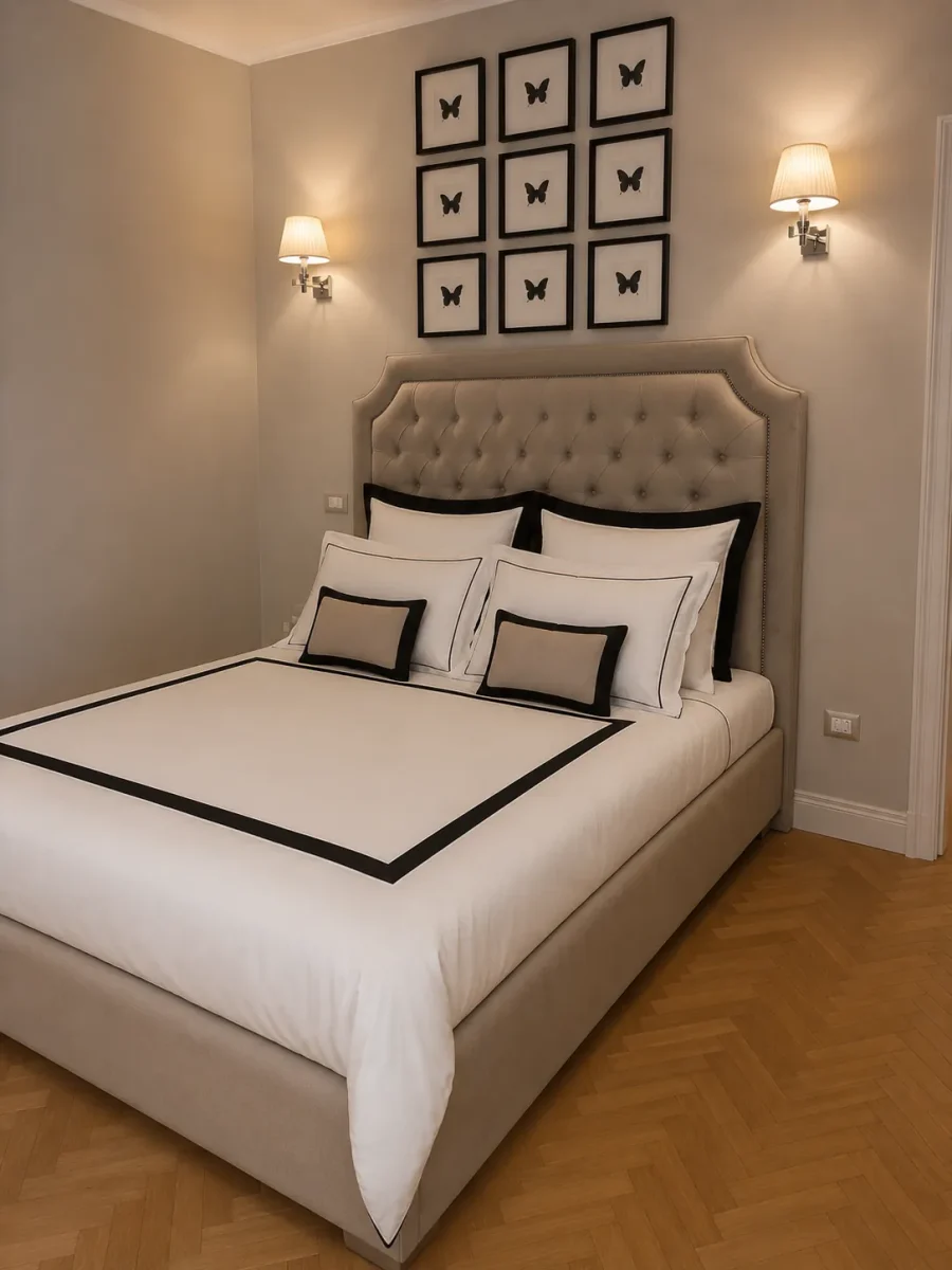 Camera con letto matrimoniale, testiera capitonne tortora e nove quadretti a farfalla sopra il letto, parquet a spina di pesce