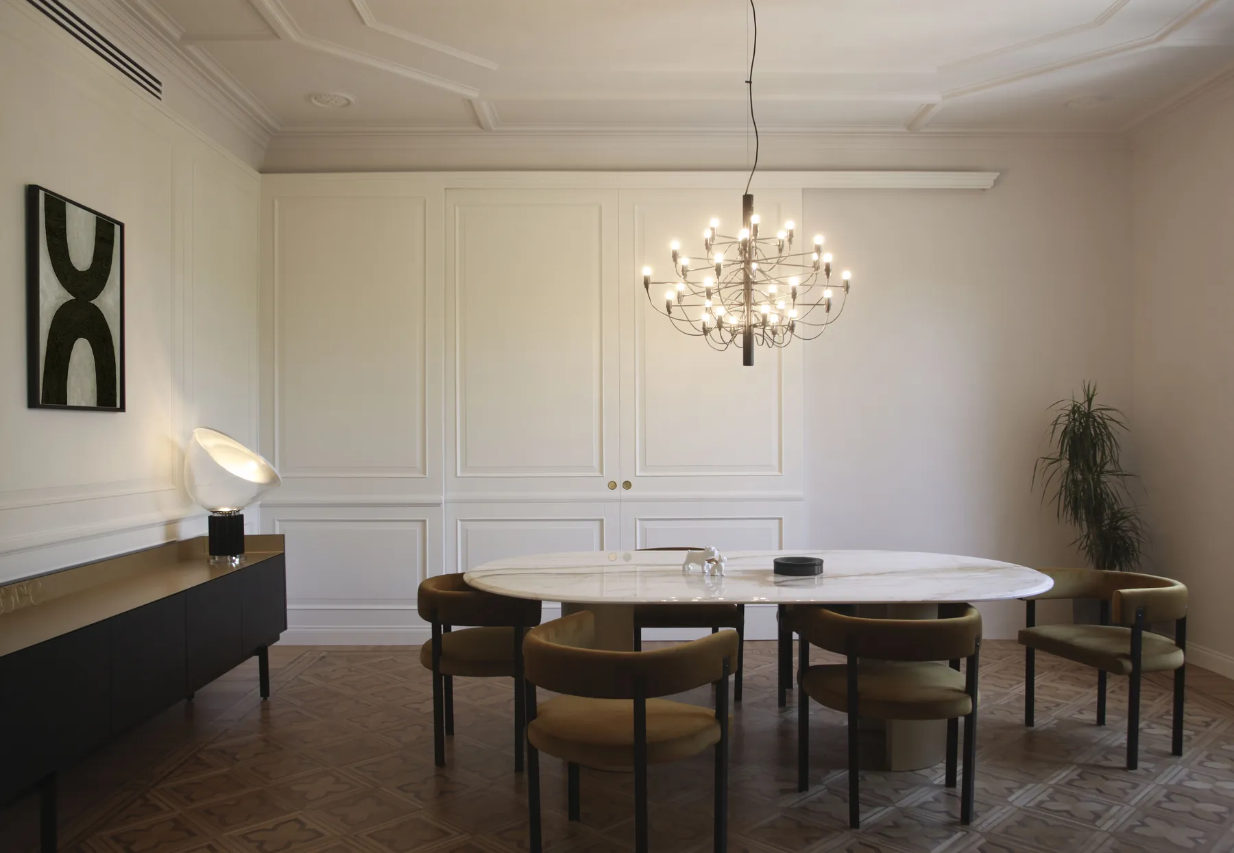 Sala da pranzo con tavolo ovale dal piano in marmo calacatta, sedie in velluto e lampadario a cascata sotto la boiserie laccata