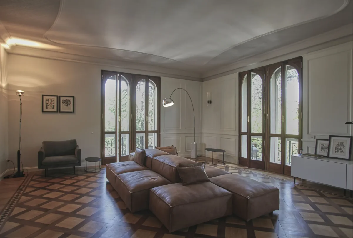 Divani modulari in pelle marrone nel salone, tra le finestre ad arco e la boiserie bianca, sul parquet in rovere intarsiato
