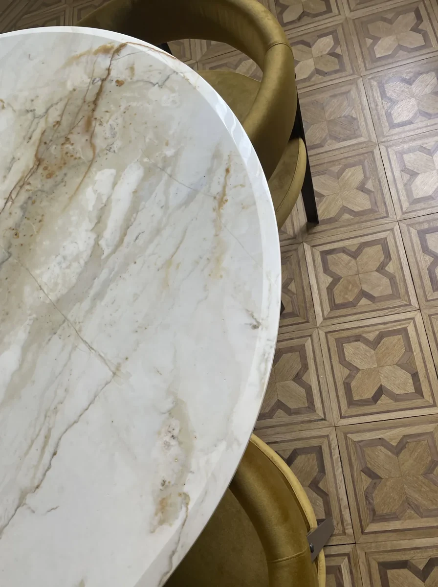 Dettaglio del piano ovale in marmo calacatta sul parquet in rovere con intarsi geometrici