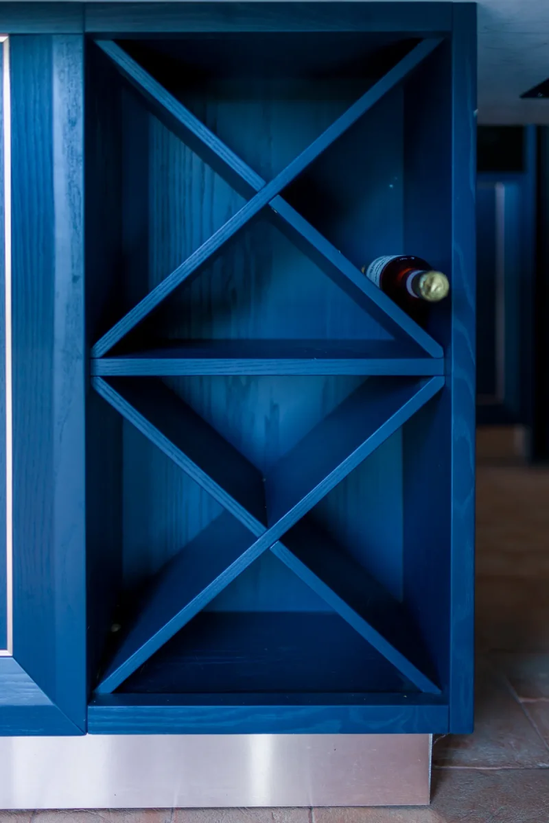 Cantinetta a X in rovere laccato blu integrata nel fianco dell'isola, con bottiglia di vino
