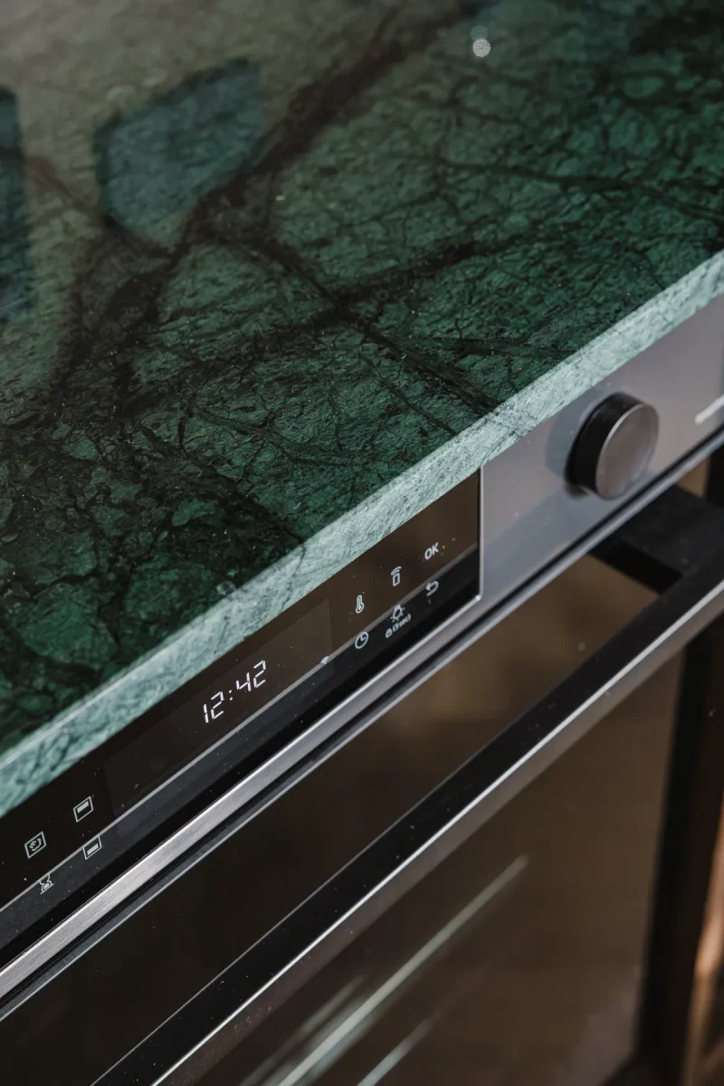 Forno nero a incasso con display acceso, sotto lo spigolo del piano in marmo verde alpi.