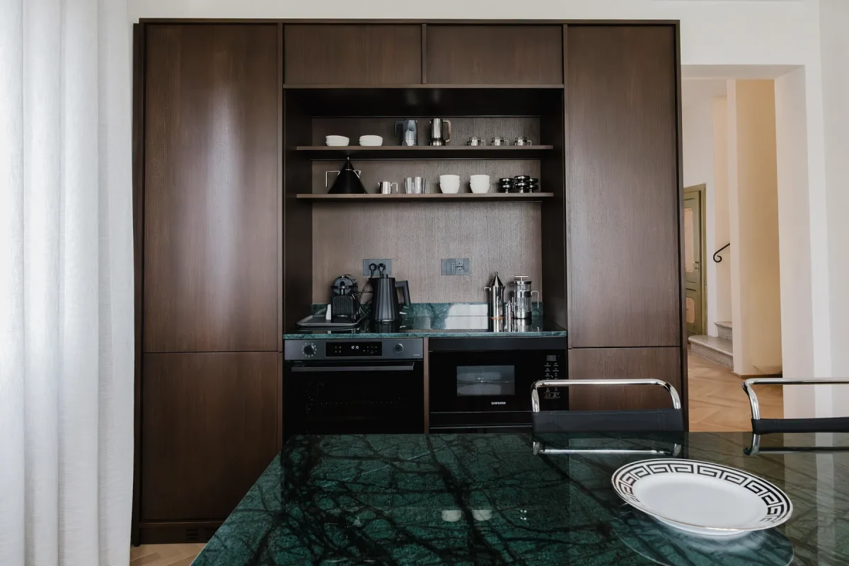 Credenza a giorno in legno wengè con stoviglie sui ripiani e piano in marmo verde alpi in primo piano.