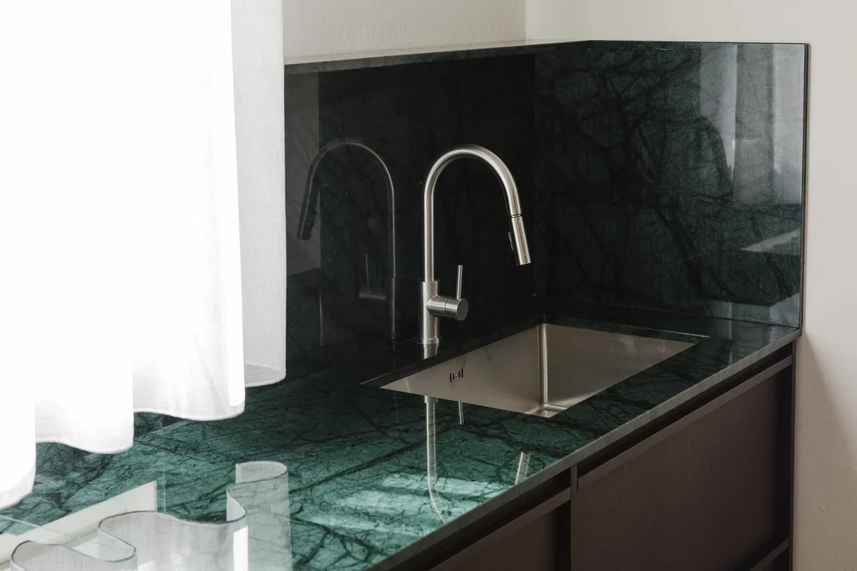Lavello in acciaio sottotop con rubinetto a canna alta, tra piano e alzatina in marmo verde alpi.